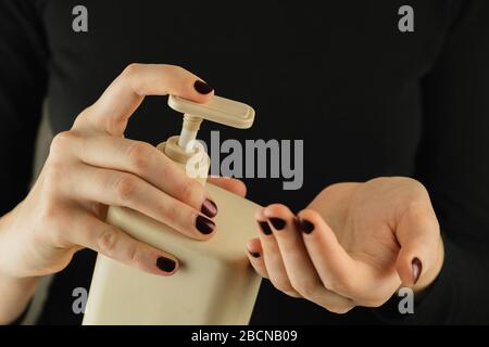 Bottle of hand sanitizer or soap in female hands, close-up view. Low-key image of personal hygiene, cleaning and self-care generic products Stock Photo