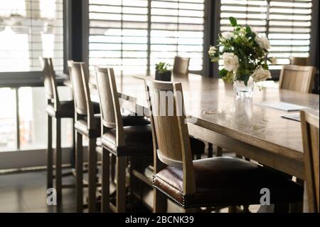 Empty wooden chairs with leather padding are set around tables in restaurant. Cafe closed during covid-2019 quarantine. Stock Photo