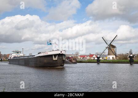 Ship sails in channel 'Gouwekanaal' near Gouda, Holland with traditional windmill on the bank of the water. Stock Photo