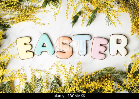 Easter letters gingerbread on bright table with mimosa flowers. Happy holiday top view background. Preparations concept Stock Photo