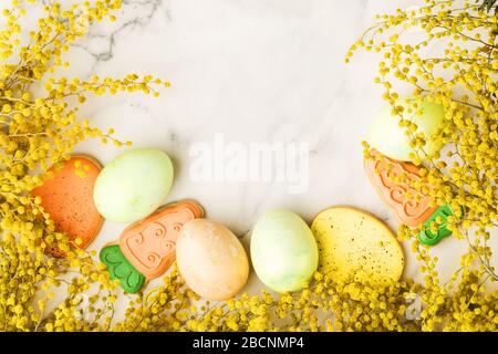 Colorful painted eggs with holiday gingerbread and mimosa flowers on marble table. Happy Easter concept. Top view background with copy space Stock Photo