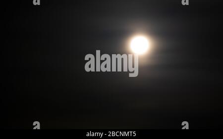 The full moon illuminates the earth. The moon on the night sky in a haze of clouds. Stock Photo