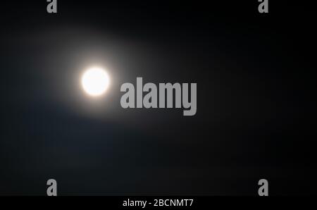 The moon on the night sky in a haze of clouds. The full moon illuminates the earth. Stock Photo