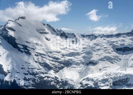 aerial, from a glider, of snow landslides and little puffy cloud wisps  at Mt. Avalanche, shot in bright spring light from east, Otago, South Island, Stock Photo