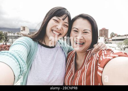 Happy asian mother and daughter taking selfie portrait photo for mother's day fest - Family people having fun with technology trends - Love and summer