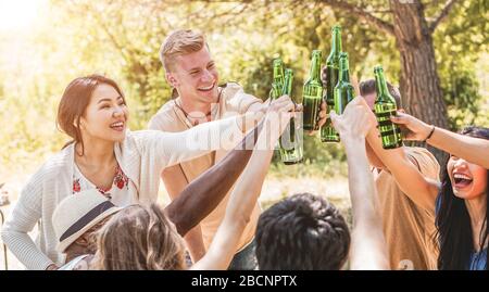 Happy multiracial friends cheering with beers at barbecue meal outdoor - Group of people having fun at bbq lunch - Summer lifestyle, friendship and fo Stock Photo