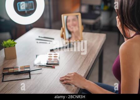 Young influencer woman creating social media videos with smartphone camera while putting on make up - New digital jobs trends, technology, cosmetics a Stock Photo