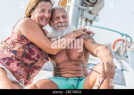 Senior couple on sailboat during luxury ocean trip vacation - Old trendy people having fun on exclusive holiday - Travel and joyful elderly concept -