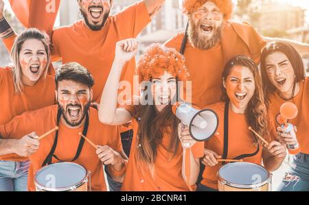 Orange sport fans screaming while supporting their team out of the stadium - Football supporters having fun at competion event - Champions and winning Stock Photo