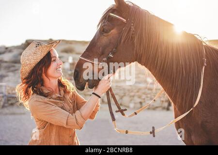 Young farmer woman playing with her bitless horse in a sunny day inside corral ranch - Concept about love between people and animals - Focus on girl f