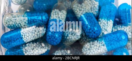 Many blue white two color transparent supplement pills with granules, medication in a see through bottle, blur. Lots of big vitamin capsules visible Stock Photo