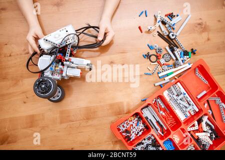 From above view of hands of incognito kid holding robot and working on project, details in box. Colorful pieces from building kit for children on tabl Stock Photo