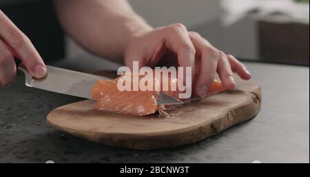 man hands slicing salted trout with knife on olive wood board Stock Photo