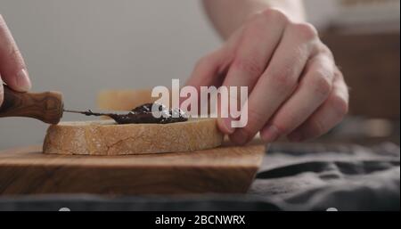 man spreading chocolate nut spread on ciabatta slice on olive board Stock Photo