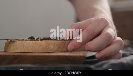 man spreading chocolate nut spread on ciabatta slice on olive board Stock Photo