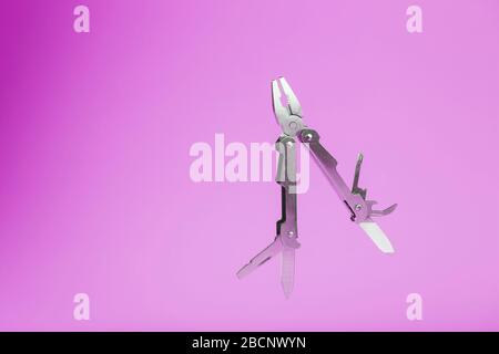 Multitool is a multi-functional tool on a pink background. The concept of an open, flying multi-tool with free space. Stock Photo