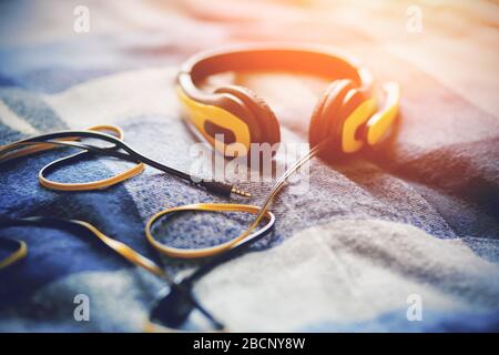 Yellow headphones with a microphone lie on a blue plaid blanket, illuminated by bright sunlight. Music and inspiration. Stock Photo