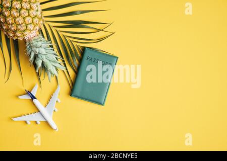 Summer vacation or travel concept. Flat lay palm leaf, pineapple, airplane toy and passport on yellow table. Top view summer background with traveler Stock Photo