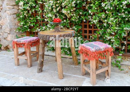 Two wooden stools and a small table on the background wall with flowering jasmine. Oriental style Stock Photo