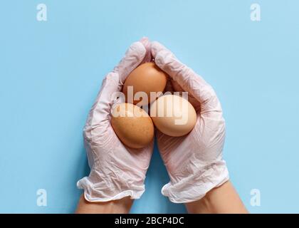 Hands in gloves keeping eggs over light blue background top view Stock Photo