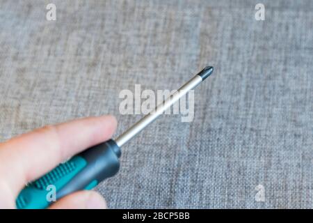 Various screwdrivers on a gray background. Repair concept. Close up of male holding hand instrument for repairing and fixing at home. Stock Photo
