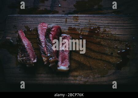 Sliced medium rare beef steak on a wooden cutting board with blood top view unhealthy food Stock Photo