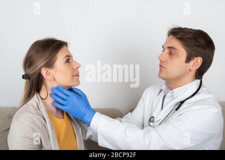 Young male doctor consulting female patient with influenza symptoms at home Stock Photo