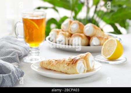 Puff pastry horn with white cream. Fresh dessert roll with cream or meringue and tea with lemon on a light background. Delicious and beautiful meringu Stock Photo