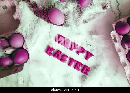 Creative bright composition with festive atmosphere. Easter holiday decorations on marble background. Fluffy white feathers and painted purple eggs in Stock Photo