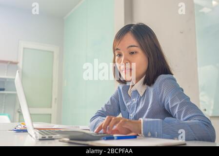 Young Asian accountant using calculator and working on computer Stock Photo