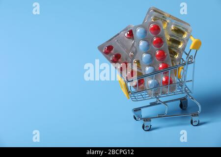 Shopping cart filled with pills. Blue background. Concept: full set of medicines in the store. Copy space for text. Medical, commercial. First aid kit Stock Photo