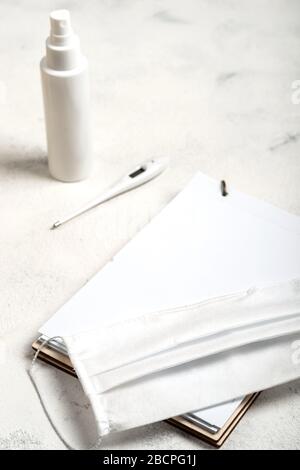 Notebook with place for text and surgical mask, hand sanitizer and digital thermometer on the white background. close-up. Stock Photo