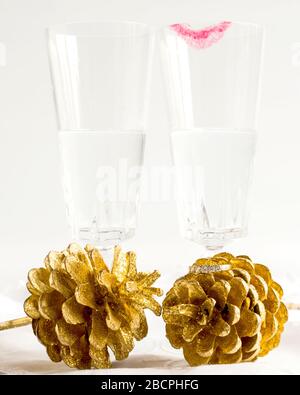 Two champagne glasses, one with lipstick, behind two gold fern cones. Diamond ring placed on one cone. Celebrating engagement, civil ceremony, wedding. Stock Photo