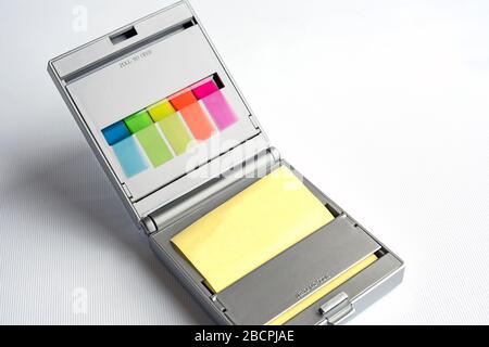 Silver dispenser of yellow postit notes and multi coloured sticky index highlighters against a white background Stock Photo