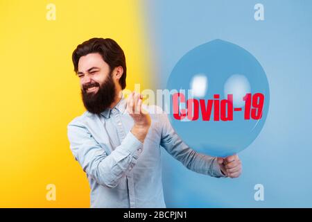 Man holding needle over blue air balloon with inscription COVID-19, a moment before bubble burst, epidemic end concept Stock Photo