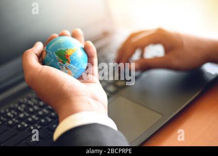 Business man holding earth globe model in hand and use a laptop / Business technology global and around the world concept Stock Photo