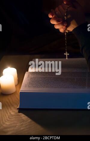 A candle, a bible and a cross a rosary on a wooden table Stock Photo