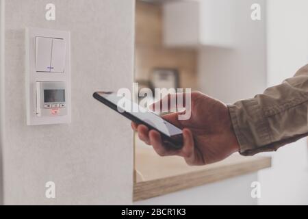Smartphone connecting to floor heating controller in kitchen. Remote home control system on a smartphone. Stock Photo