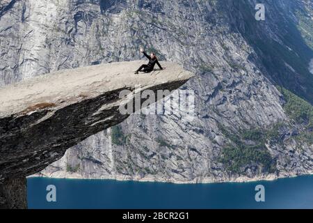 Adult woman lying on Trolltunga cliff on his back. Taking selfie picture with smartphone. Norway, Scandinavia Stock Photo