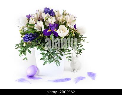 Easter decorations. Spring flowers with an Easter egg and a rabbit on a white background. Copy space. Side view. Stock Photo