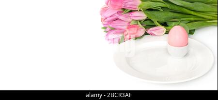 Easter table setting with spring flowers tulips and a pink Easter egg on a white background. Banner. Copy space. Side view. Stock Photo