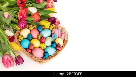 Happy easter concept. Easter eggs in a basket with a bouquet of tulips on a white background. Copy space. Stock Photo