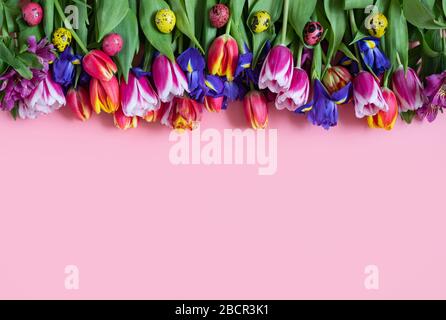 Easter frame with spring flowers and colorful quail eggs on a pink background. Happy Easter concept. Space for text. Top view, flat lay. Stock Photo