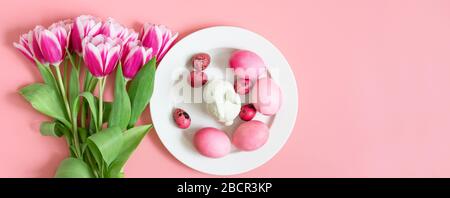 Easter holiday pink table setting with eggs, rabbit and a bouquet of tulips. Banner. Copy space, top view, flat lay. Stock Photo