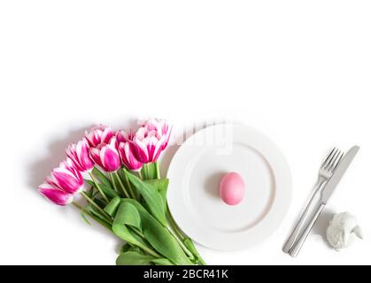 Easter holiday table setting with pink chicken egg, rabbit and tulip flowers on a white background. Copy space, top view, flat lay. Stock Photo