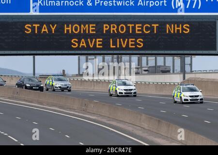 Coronavirus UK - measures in Scotland - Police vehicles passing under 'Stay Home Protect NHS Save Lives' sign in Glasgow