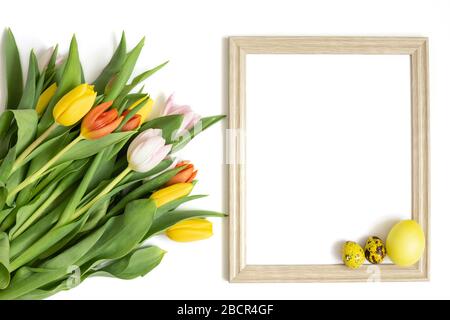 Easter frame with a bouquet of tulip flowers and yellow eggs on a white background. Copy space, top view, flat lay. Stock Photo