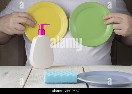 A young man in an apron washes dishes in the kitchen. A man holds a washed plate Stock Photo