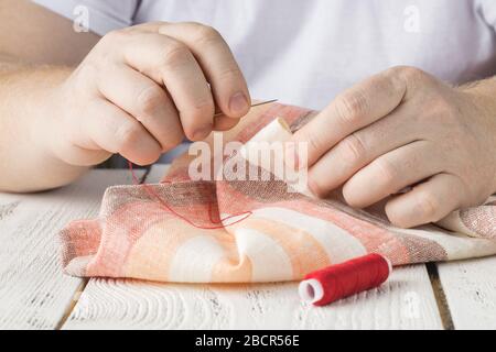 people, needlework, sewing and tailoring concept - tailor man with thread in needle stitching fabric. Hands sewing with a needle and thread. Fingers p Stock Photo