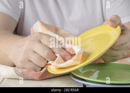 A young man in an apron washes dishes in the kitchen. A man holds a washed plate Stock Photo